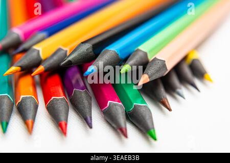 A pile of colorful pencils in various shades is on a white surface, showing sharp tips for drawing and coloring activities. Stock Photo