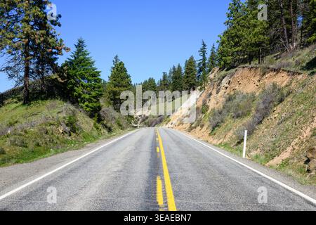 Two lane rural road passing cutting on ridge in Eastern Washington in springtime Stock Photo