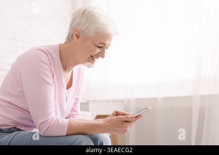 Cheerful senior woman using her smartphone at home Stock Photo