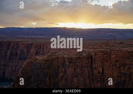 Sun setting behind a plateau above a deep canyon with sheer red rock cliffs and power lines crossing the desert landscape. Stock Photo