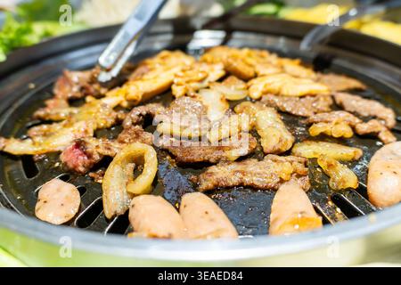 Sizzling Korean BBQ grill with marinated beef, pork belly, sausages, and onions cooking on hot Stock Photo