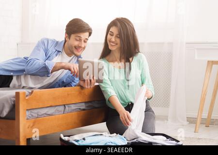 Couple Enjoys Time Together While Folding Laundry and Using a Tablet in Bright Room Stock Photo