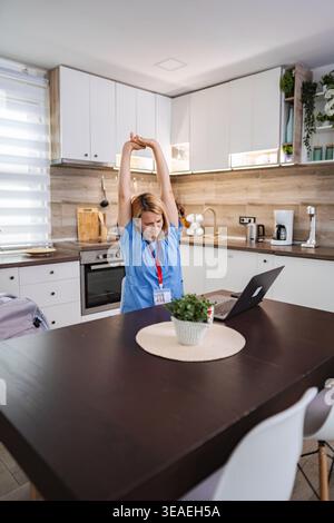 Female Doctor Stretching While Working From Home in Kitchen Stock Photo