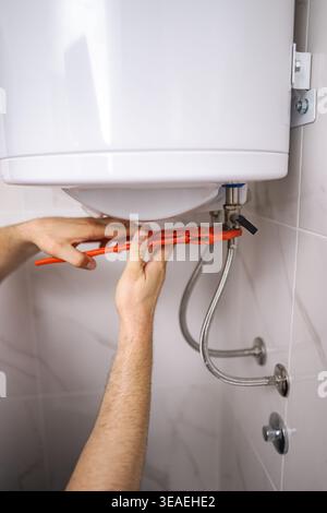 Plumber working on water heater using adjustable wrench in bathroom Stock Photo