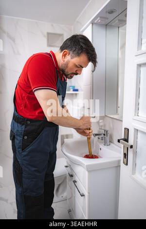 Plumber working using a plunger to unclog a bathroom sink Stock Photo