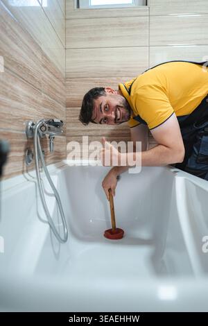 Plumber unclogging a bathtub drain using a plunger and giving thumbs up Stock Photo