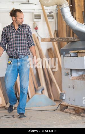 Woodworker operating planing machine in busy workshop Stock Photo