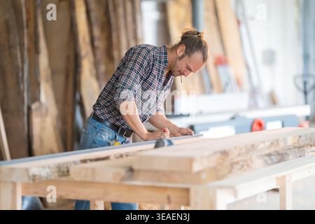 Carpenter marking wooden plank with ruler in workshop Stock Photo