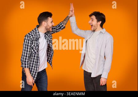 Two Friends Sharing a High Five in a Bright Orange Setting With a Joyful Atmosphere Stock Photo