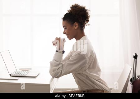 Young Woman Working Thoughtfully at a Desk With a Laptop in a Bright, Modern Room Stock Photo