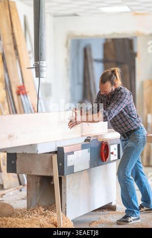 Woodworker flattening wood plank using jointer machine Stock Photo