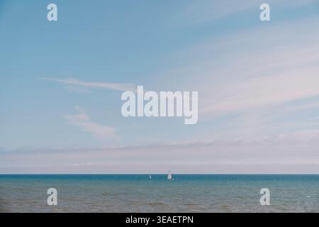 Peaceful ocean with distant vessels. Calm sea stretching to horizon with sailboats beneath pastel sky colors Stock Photo