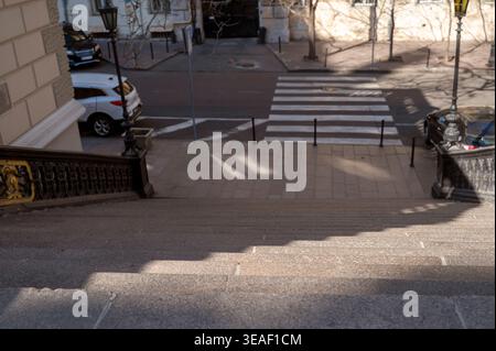 Outdoor granite steps descending to a pedestrian crossing in a city center under sunlight. Stock Photo