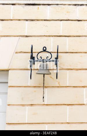 Vintage Iron Bell Mounted On Beige Stone Wall With Rope Pull And Rustic Bracket Stock Photo
