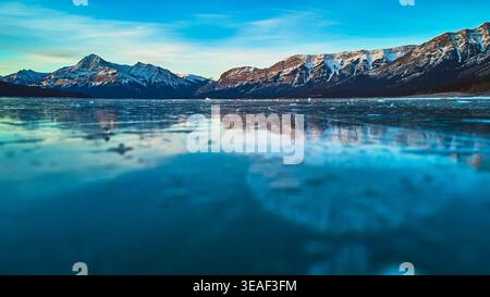 Frozen Lake Surface and Snow Capped Mountains at Sunrise in Winter Stock Photo
