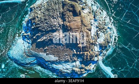 Aerial Frozen Rocky Outcrop with Cracked Ice Patterns on Winter Lake Top Down Stock Photo