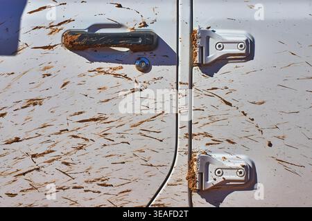 Muddy White Vehicle Door Close Up with Handle and Hinges in Harsh Sunlight Stock Photo