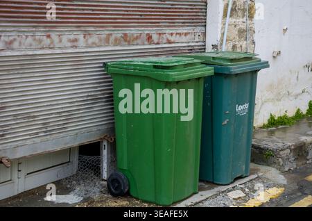 Two green garbage bins beside a weathered wall Stock Photo