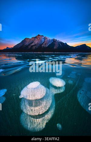 Frozen Methane Bubbles and Mountain Reflections on Winter Lake at Sunset Stock Photo