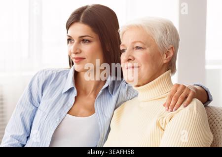 Younger Woman and Elder Woman Sitting Together in Comfortable Indoor Setting Sharing a Moment Stock Photo