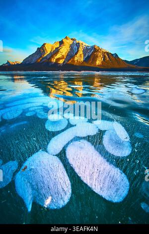 Frozen Methane Bubbles Under Clear Ice and Sunlit Mountain Winter Landscape Stock Photo