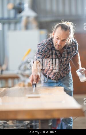 Carpenter applying protective epoxy resin to wood surface Stock Photo