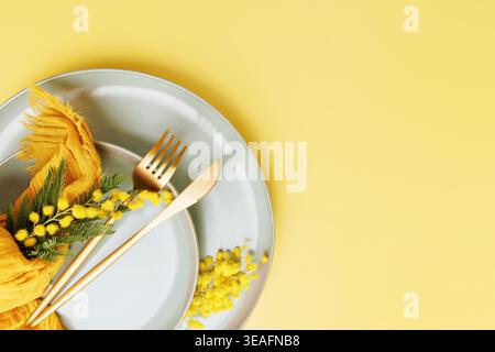 Spring table setting with mimosa flowers and copy space on pastel yellow Stock Photo