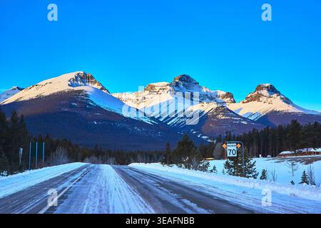 Winter Highway and Snowy Mountain Peaks with Forest in Alberta Stock Photo