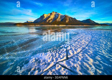 Frozen Lake Cracks and Snow Patterns with Majestic Mountains in Winter Light Stock Photo