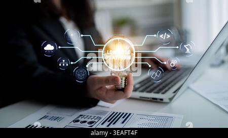 Business Professional Holding Light Bulb with Digital Low-Code Platform Icons while Working on Laptop in Modern Office Setting Quark. Stock Photo