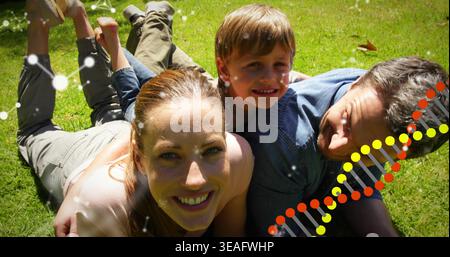 Lying family trio wearing casual summer clothes smiling on backyard lawn, with DNA helix overlay Stock Photo