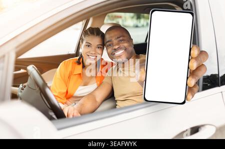Smiling black couple sitting in car, holding smartphone with blank screen Stock Photo