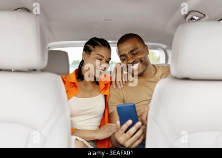 Young black couple using smartphone together in car, smiling and browsing content Stock Photo