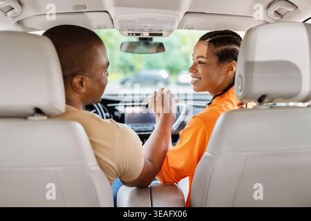 Young black couple holding hands inside a car, smiling and connecting emotionally Stock Photo