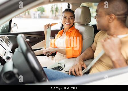 Smiling Black couple fastening seatbelts while sitting in car, ready for trip Stock Photo