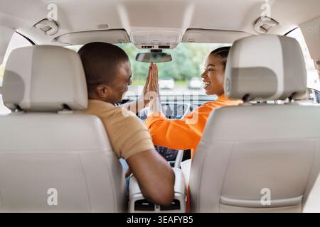 Black couple giving high five in car, smiling woman celebrating with man Stock Photo