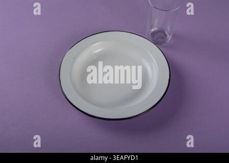 Minimalist setup featuring white enamel plate and glass on a textured purple background. Clean, soft lighting. Promotes healthy lifestyle, mindful eat Stock Photo