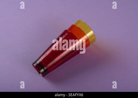 Three translucent stacking cups in red, orange, and yellow. Isolated on purple backdrop. Clean studio lighting highlights smooth textures, copy space. Stock Photo