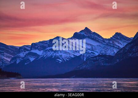Winter Sunset Over Frozen Lake and Snowy Mountain Peaks with Vibrant Sky Stock Photo