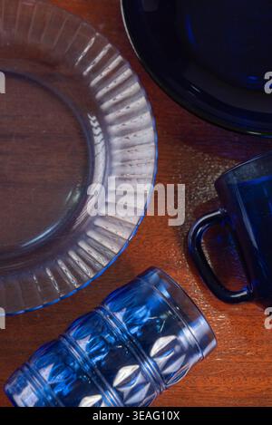 Glassware still life on wooden surface. Blue plates and cups create balanced composition. Focus on textures, color harmony. Low-key lighting enhances Stock Photo