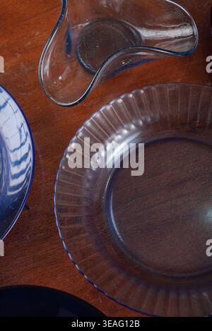 Arrangement featuring translucent blue glass plates and a bowl on a dark wood surface. Soft illumination accentuates the textures. Suitable for culina Stock Photo
