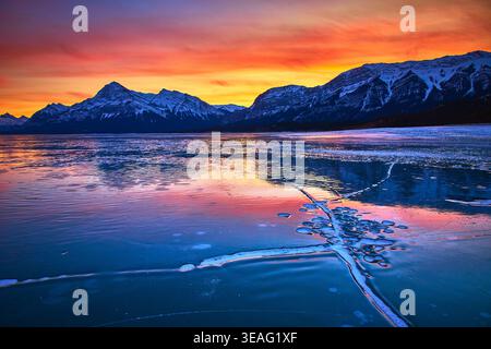 Vibrant Winter Sunset Over Frozen Lake With Cracked Ice and Snowy Mountains Stock Photo