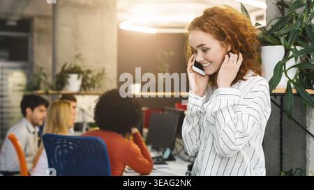 Young Woman Smiling While Talking on Phone in a Modern Office Space During Working Hours Stock Photo