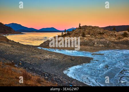 Frozen Lake Ice Cracks Rocky Shoreline and Sunset Sky in Winter Stock Photo