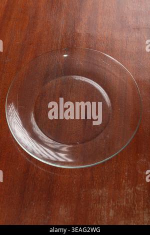 Minimalist still life features clear glass plate displayed center frame on rustic wooden surface. Clean food presentation mock up with studio lighting Stock Photo