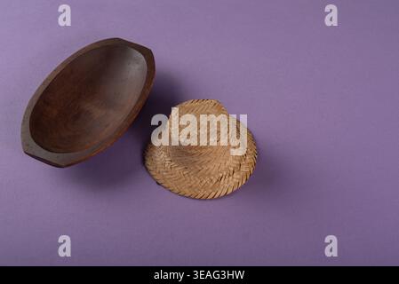 Studio shot features straw hat and wooden bowl isolated on purple background. Soft light reveals woven texture of hat and smooth wood grain. Ideal for Stock Photo