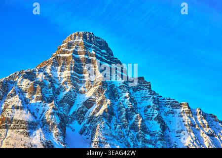Snow Covered Mountain Peak with Blue Winter Sky and Rugged Rocky Texture Stock Photo