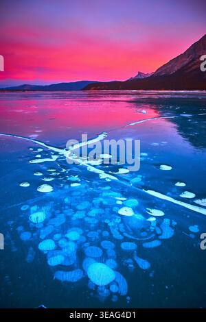 Frozen Lake Ice Bubbles at Sunset with Mountains and Vibrant Winter Sky Stock Photo