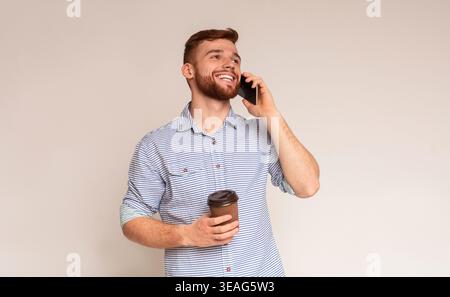 Young bearded man holding cup of coffee and talking on phone Stock Photo