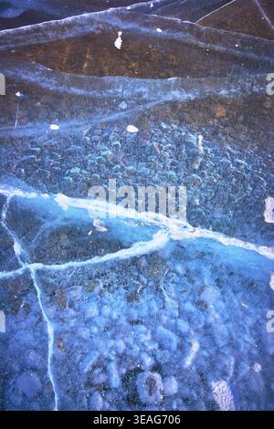 Frozen Ice Cracks and Bubbles Over Rocky Lakebed Winter Texture Close Up Stock Photo